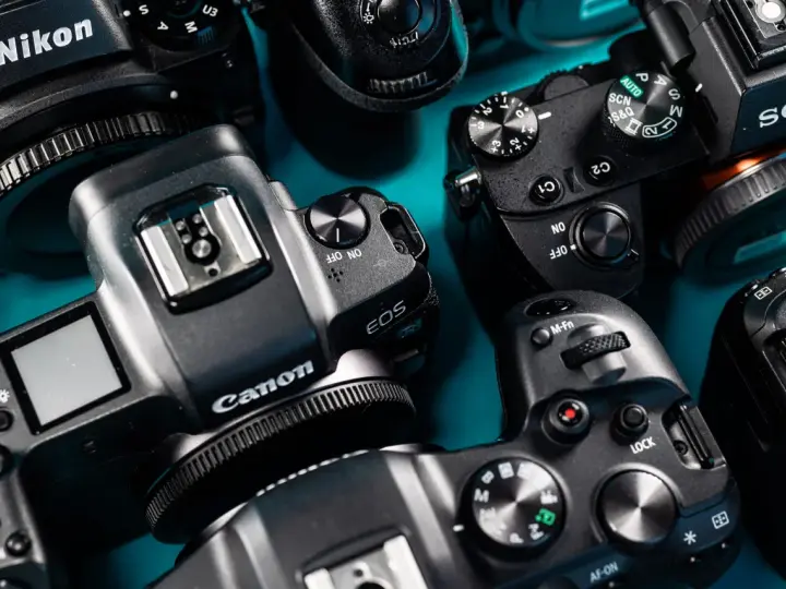 Zbliżenie na kilka aparatów cyfrowych marek Nikon, Canon i Sony ułożonych na niebieskim tle.