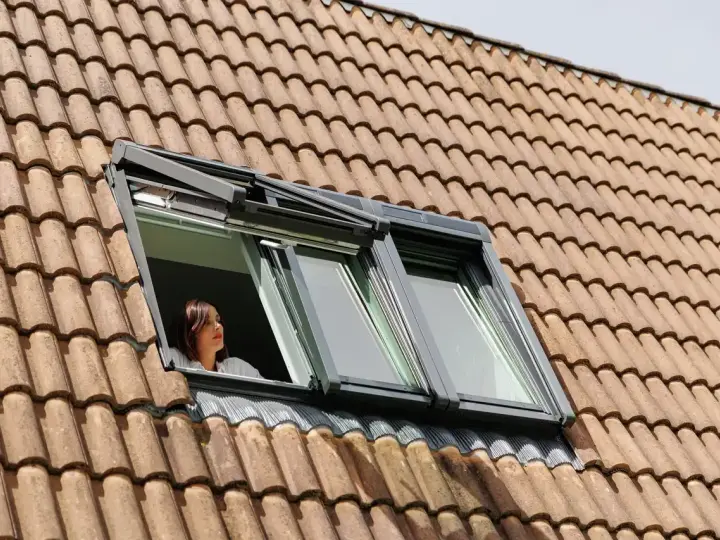 Donna guarda fuori da una finestra sul tetto, un esempio di come isolare il tetto dall'esterno per un maggiore comfort.
