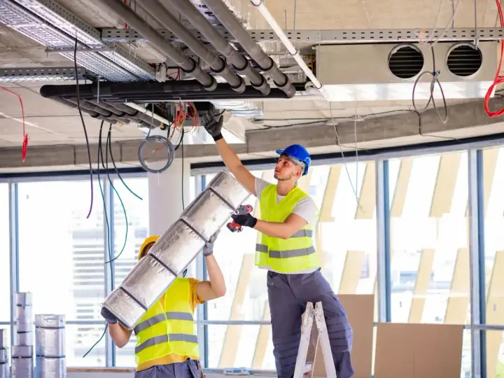 Dwóch pracowników montuje systemy HVAC, instalując izolację na rurach. To kluczowy element zapewniający komfort cieplny.