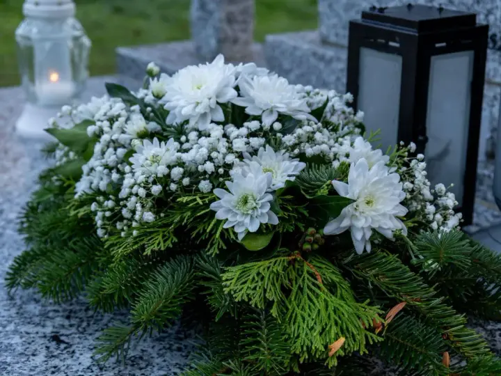 Białe kompozycje z chryzantem i iglastymi gałązkami na grobie, symbol pamięci na Wszystkich Świętych.