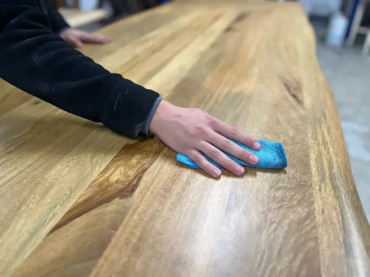 Main d'une personne passant un chiffon bleu sur une table en bois, montrant comment nettoyer une table en bois.