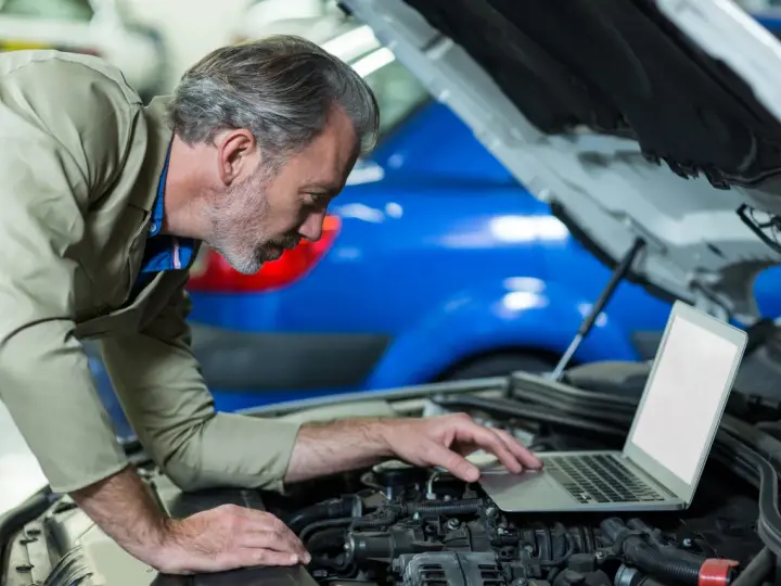 Mechanik z laptopem przy otwartej masce samochodu.