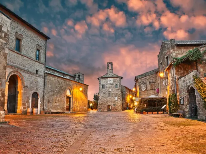 Piazza medievale illuminata al tramonto, con edifici in pietra e un campanile. Un luogo incantevole dove scoprire cosa vedere.