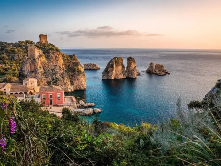 Traumhafte Küstenlandschaft mit Felseninseln, einem alten Turm und einem roten Haus. Perfekt für ein Auslandsjahr in Italien.