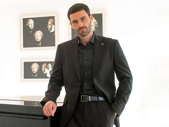 Uomo elegante in completo nero, camicia nera uomo abbinamento perfetto. Sfondo con quadri di busti classici.