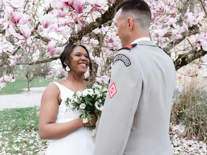 Un couple rayonnant lors de leur mariage militaire, sous un magnolia en fleurs.