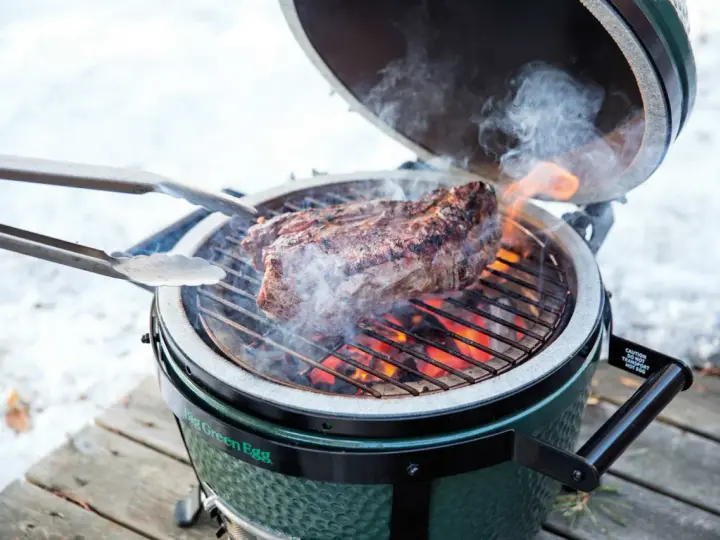 Un succulento bistec a la fiorentina cuoce sulla griglia di un Big Green Egg, circondato da fumo e fiamme.