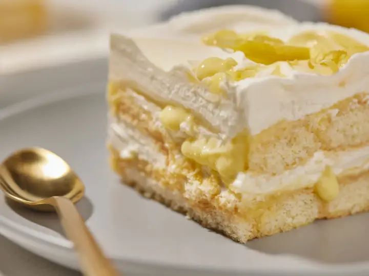 Ein Stück Zitronen Tiramisu mit cremiger Füllung und Zitronenscheiben, daneben eine goldene Löffel.