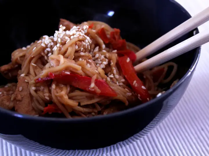 Miseczka pełna aromatycznego makaronu teriyaki z kawałkami kurczaka i papryką, posypana sezamem.