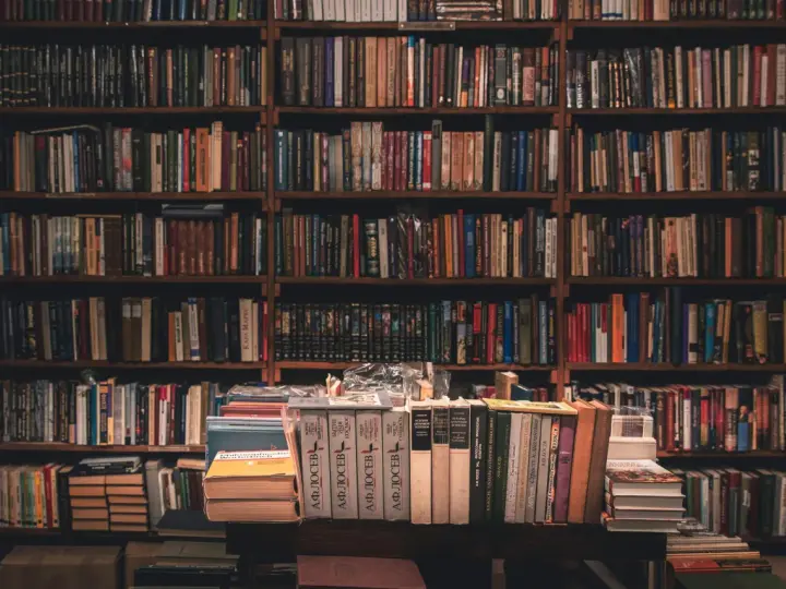 Wielka biblioteka pełna książek. Na pierwszym planie stosy książek, jedna z nich przypomina bułeczkę.