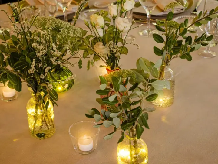 Elegante decoracion con velas y flores en jarrones de cristal, creando un ambiente cálido y acogedor para una cena especial.