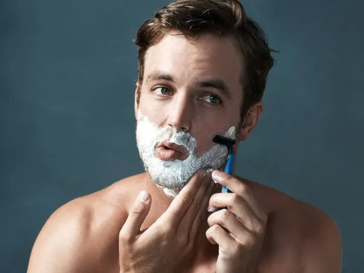 Hombre con espuma de afeitar en la cara, aprendiendo como afeitarse la barba con una maquinilla.