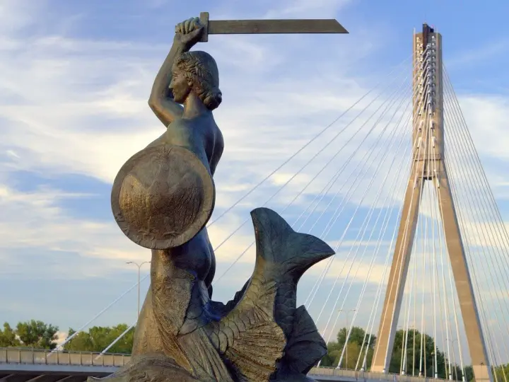 Syrenka Warszawska z mieczem i tarczą, symbol legendy o syrence warszawskiej, na tle nowoczesnego mostu.