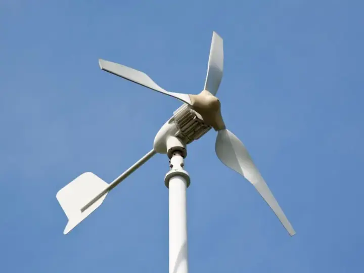 Mała turbina wiatrowa z białymi łopatami i ogonem, idealna jako jaka turbina wiatrowa do domu, na tle błękitnego nieba.