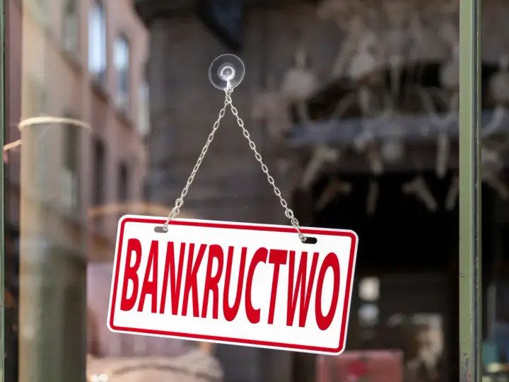 Tabliczka "BANKRUCTWO" wisząca na łańcuszku na szybie.