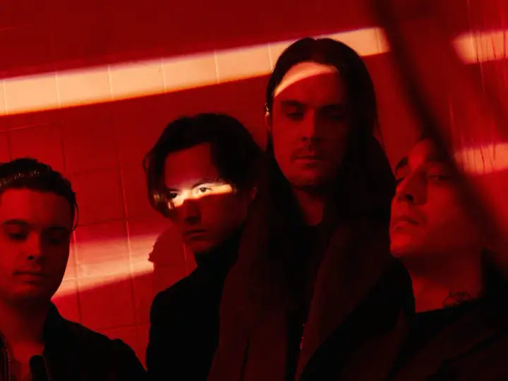 Les membres de Bad Omens posent dans une ambiance rouge intense, éclairés par des ombres dramatiques.