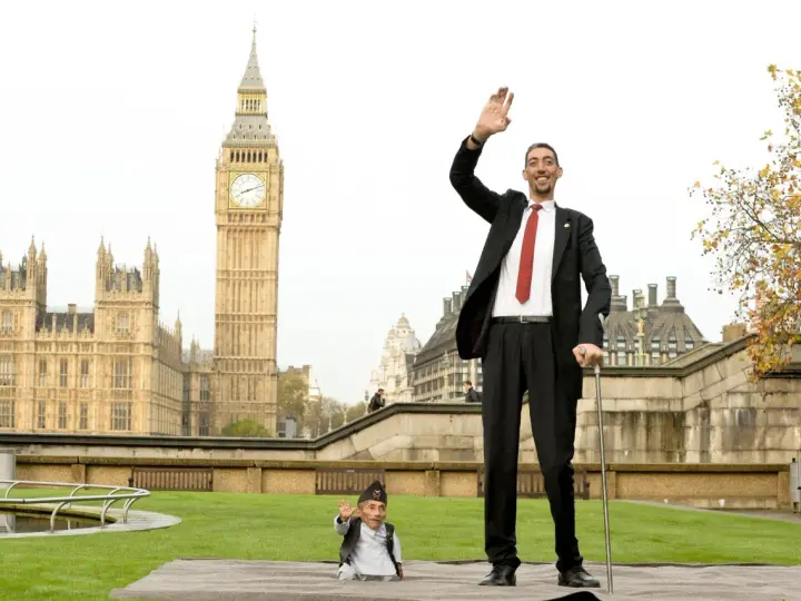 Der größte Mensch der Welt winkt vor dem Big Ben in London. Neben ihm steht ein Mann von sehr kleinem Wuchs.