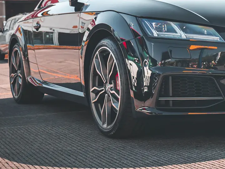 Błyszczące, czarne auto sportowe z felgami i widocznym rantem ochronnym opony.