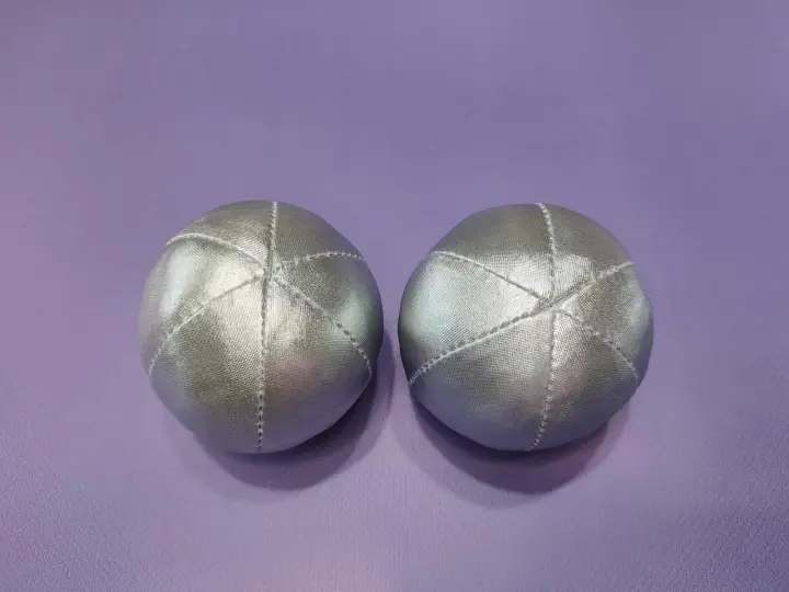 Deux balles en tissu argenté, parfaites pour un **patron gratuit balle en tissu**. Elles sont posées sur un fond violet.