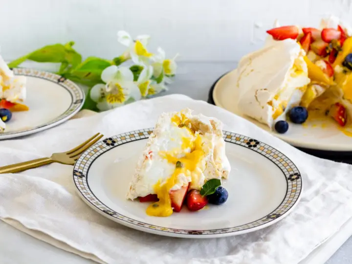 Porción de pavlova con fresas, arándanos y mango, bañada en salsa de maracuyá. Los pavlova ingredientes son visibles en este postre.