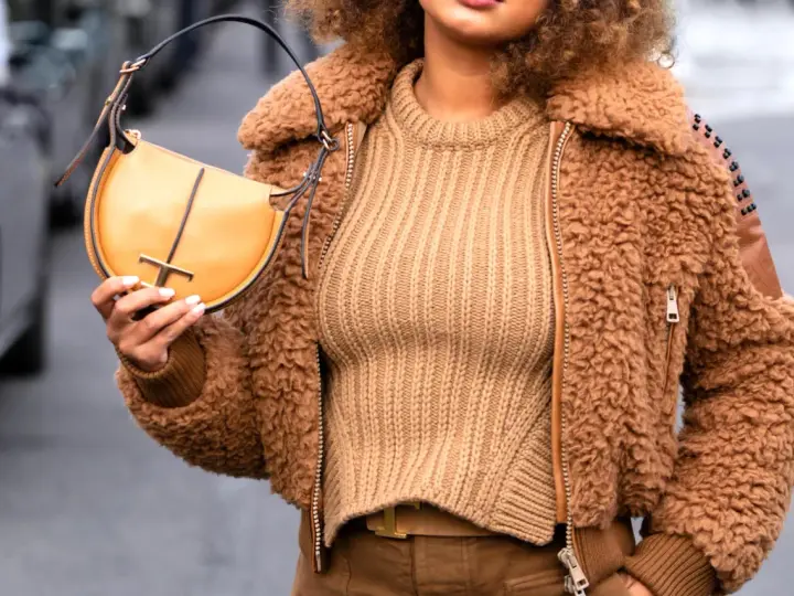 Une femme porte un pull beige côtelé, une veste en fausse fourrure marron et un sac à main jaune moutarde. Le jaune moutarde est une couleur qui va bien avec le beige.