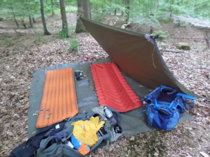 Zwei Isomatten, ein Tarp und Rucksäcke liegen bereit, um unter freiem Himmel zu schlafen.