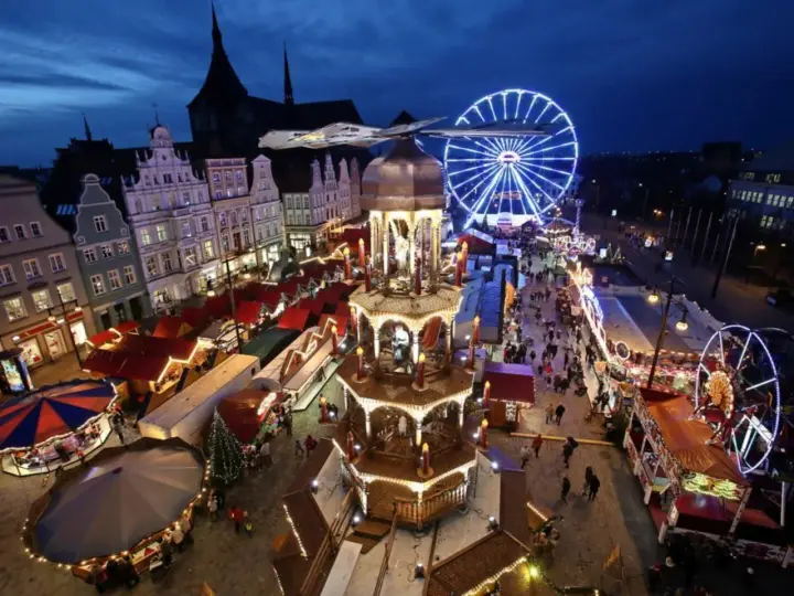 Ein beleuchteter Weihnachtsmarkt Mecklenburgische Seenplatte mit Riesenrad, Pyramide und Buden.
