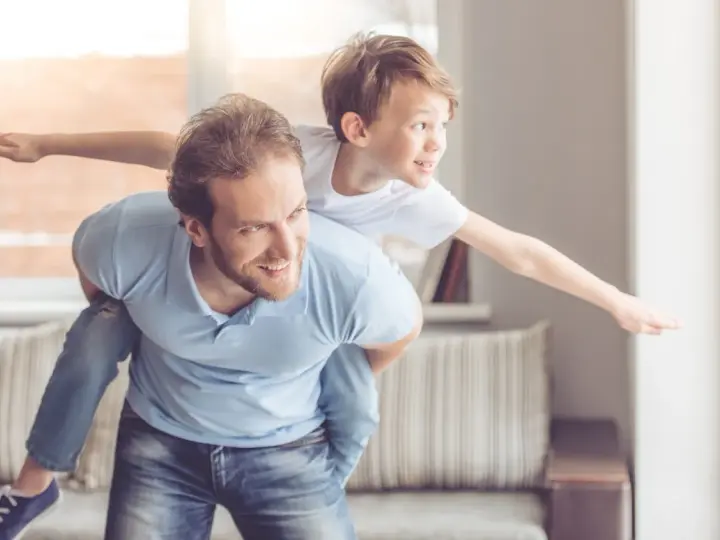 Ein Vater trägt seinen Sohn auf dem Rücken. Der Sohn streckt die Arme aus wie ein Flugzeug. Das sind meine worte an meinen sohn: Flieg hoch!