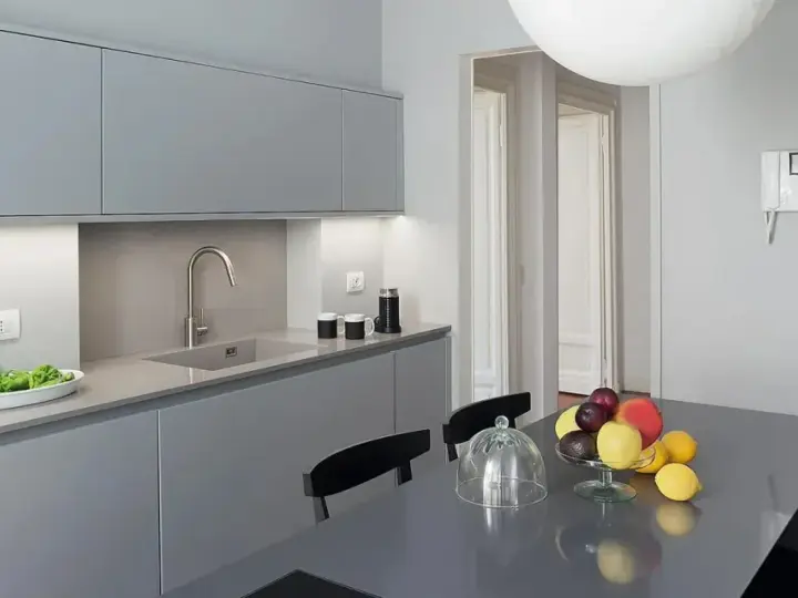 Cucina moderna con pensili e basi grigie. Il colore pareti neutro esalta la pulizia delle linee. Tavolo con frutta fresca.