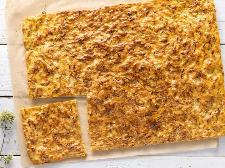 Schiacciata di zucchine e cipolle dorata e croccante, tagliata a pezzi su carta da forno.