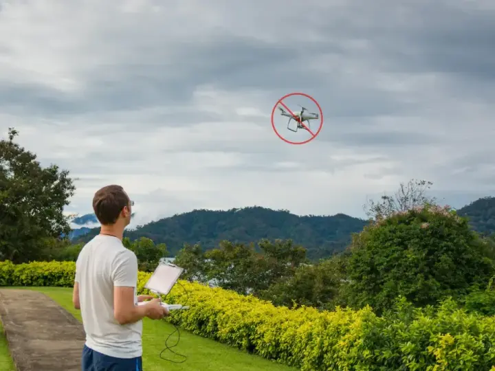 Man with drone controller looks at a drone with a "no fly" symbol, illustrating ct drone laws.