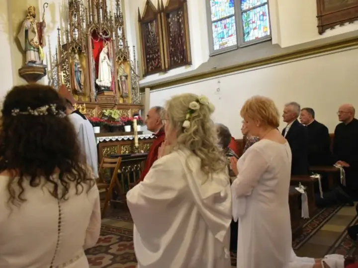Uroczystość w kościele. Kobieta w białej sukni, z kwiatami we włosach, klęczy. To moment konsekracji, ważny dla dziewicy konsekrowanej.