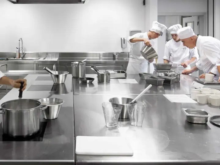 Estudiantes de cocina aprenden sobre seguridad en la cocina, preparando ingredientes en una estación de acero inoxidable.