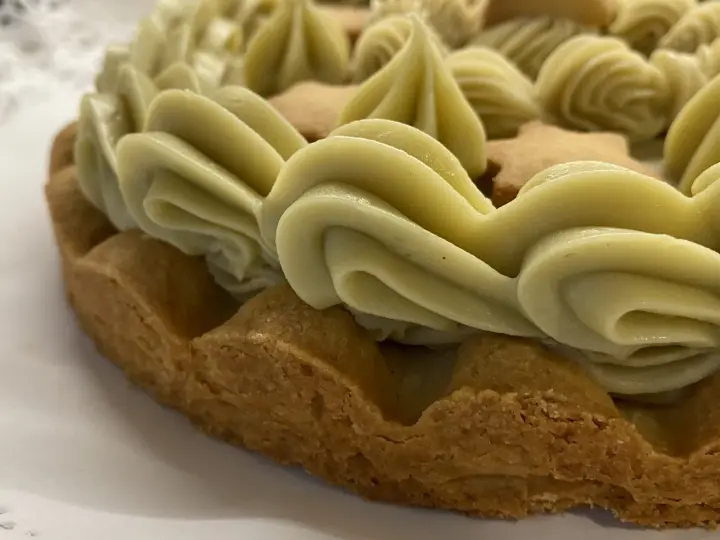Torta con bordi croccanti e un abbondante strato di ganache pistacchio, decorata con biscotti a forma di stella.