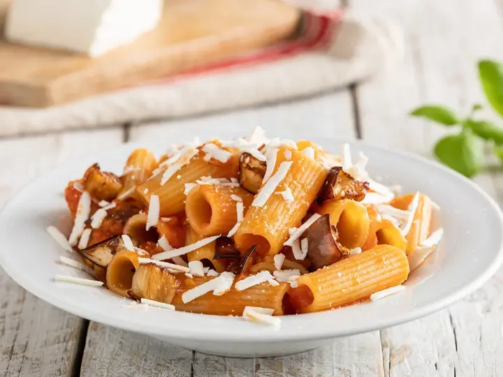 Piatto di pasta alla norma con rigatoni, melanzane fritte, pomodoro e ricotta salata grattugiata.