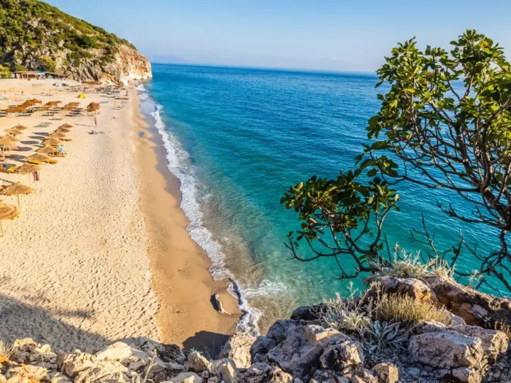Piękna plaża w Albanii, gdzie ceny są przystępne. Słoneczny dzień, turkusowa woda i zielone wzgórza.