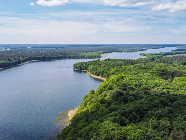 Malownicze jezioro otoczone lasem, idealne miejsce na nietypowe atrakcje Mazury. Widok z lotu ptaka na spokojną taflę wody i bujną zieleń.