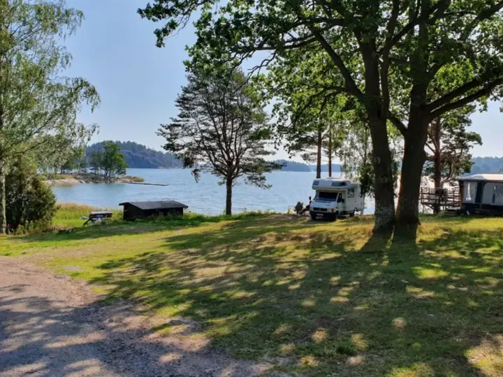 Solig dag vid vattnet på Kalvholmens camping. Husbilar och husvagnar står uppställda på gräsmattan nära sjön.