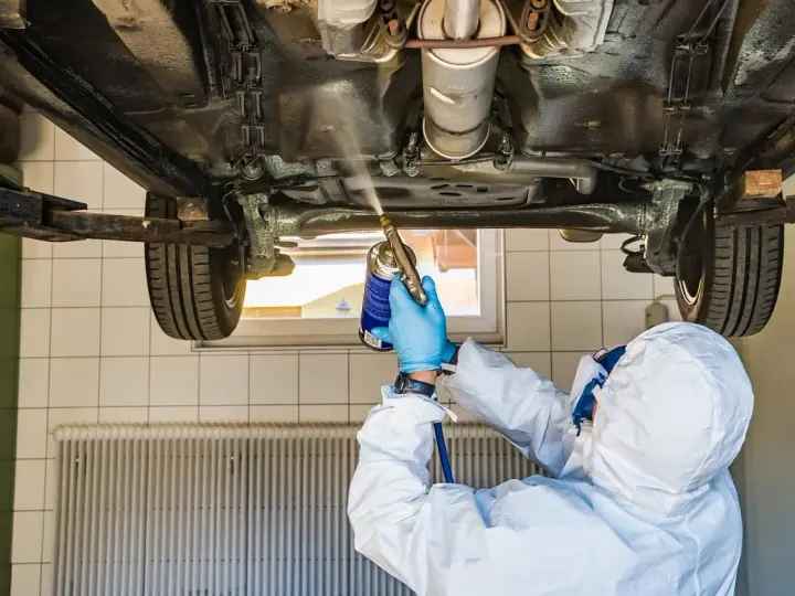 Mechanik w kombinezonie zabezpieczającym podwozie samochodu. Zastanawiasz się, ile kosztuje przegląd samochodu z gazem?