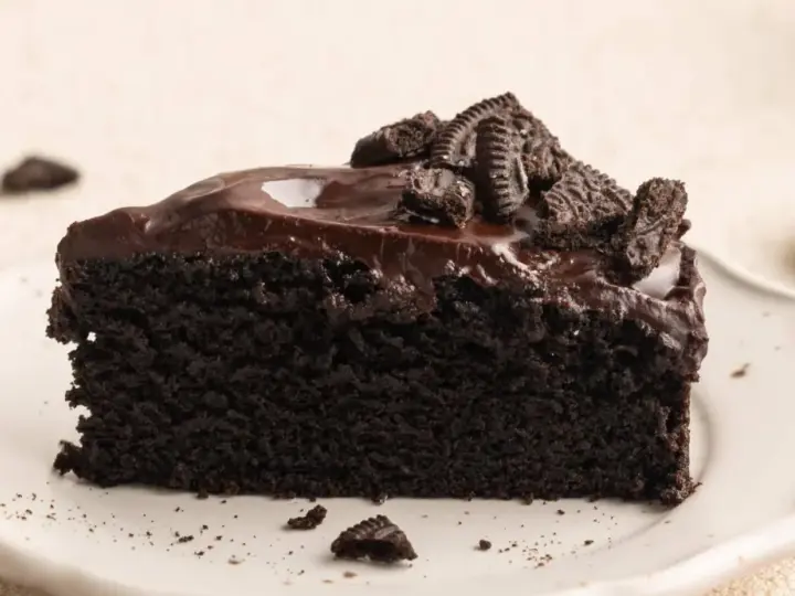 Ein saftiges Stück dunkler Oreo Kuchen mit glänzender Schokoladenglasur und zerbröselten Keksen obendrauf.