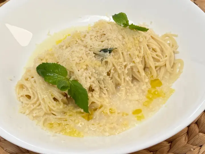 Spaghetti al limone cremosi, cosparsi di parmigiano e guarniti con foglie di menta fresca. Un piatto profumato e invitante.