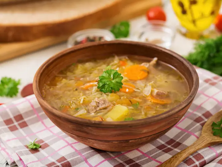 Najprostszy kapuśniak w glinianej misce, z kawałkami mięsa, ziemniaków i marchewki, ozdobiony natką pietruszki.