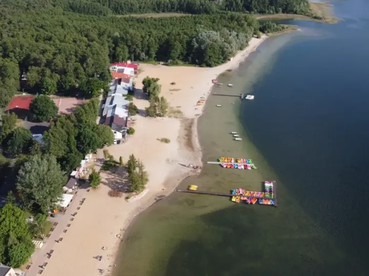 Skorzęcin jezioro z lotu ptaka: piaszczysta plaża, kolorowe rowery wodne, budynki i las.