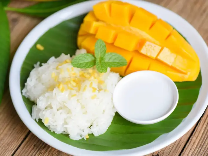 Pyszny mango sticky rice: ryż kleisty z kawałkami mango, polany mleczkiem kokosowym, udekorowany miętą.