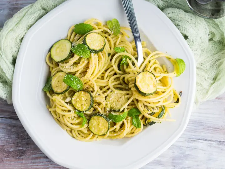 Spaghetti con zucchine cremosa, guarniti con foglie di menta fresca e parmigiano grattugiato. Un piatto leggero e gustoso.