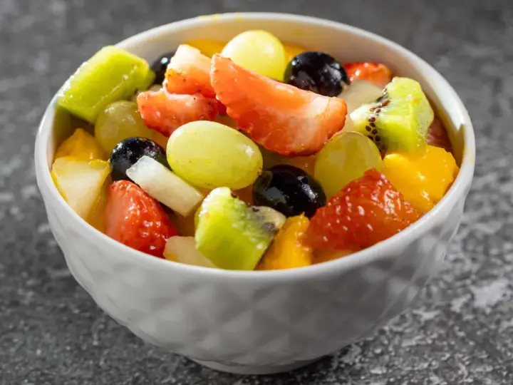 Kolorowa sałatka na imprezę: truskawki, kiwi, winogrona, mango i czarne porzeczki w białej miseczce.