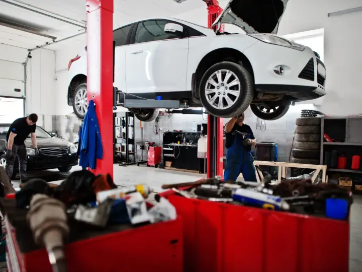 Warsztat samochodowy: biały samochód na podnośniku, mechanik w niebieskim kombinezonie.