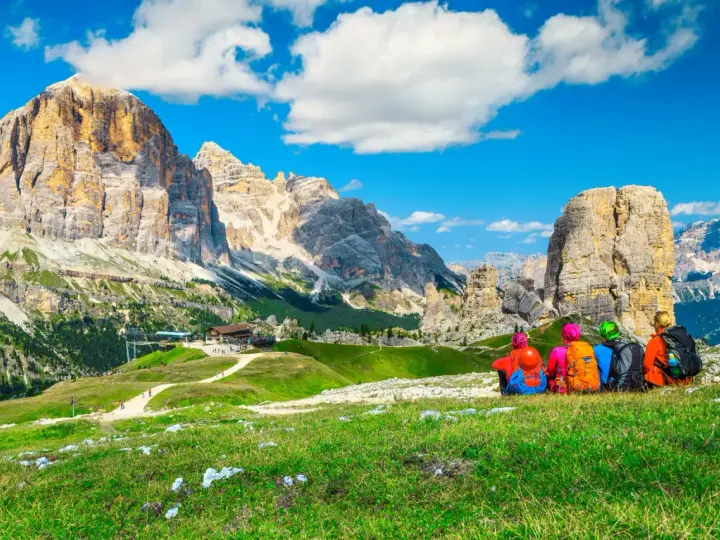 Quattro escursionisti ammirano un maestoso itinerario dolomiti, con cime imponenti e un rifugio alpino.