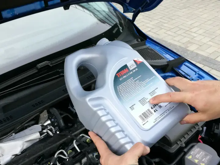 Osoba trzymająca kanister oleju silnikowego TITAN GT1 PRO C-3 SAE 5W-30 nad silnikiem. Czy można mieszać oleje silnikowe? Sprawdź specyfikacje!