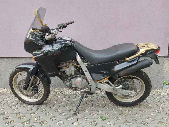 Czarny motocykl Aprilia Pegaso 650 z złotym bagażnikiem i lusterkami, zaparkowany na kostce brukowej.